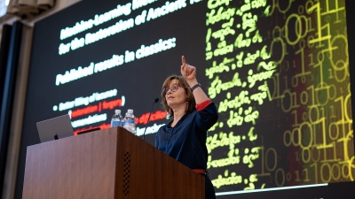 Barbara Graziosi standing at a podium pointing upwards.