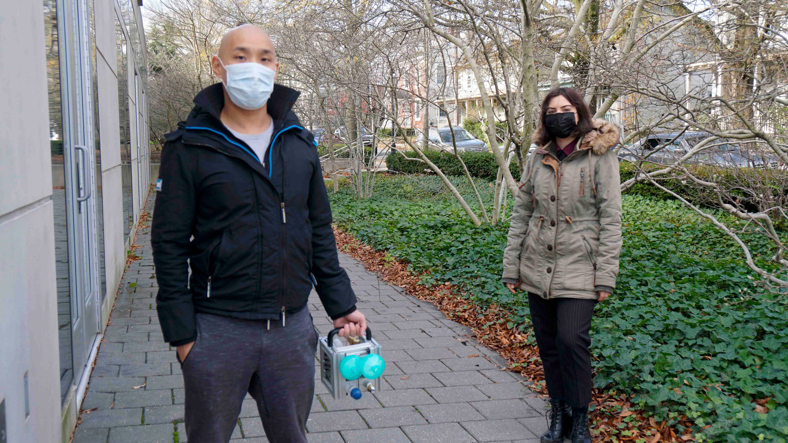 Daniel Suo and Paula Gradu standing outside of the Friend Center Building wearing masks. Daniel is holding a medical device.